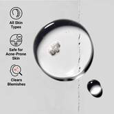 Bližinski posnetek teksture Truly-Targeted Blemish-Clearing Solution, ki prikazuje bistro tekočino s kapljicami. Besedilo poudarja primernost za vse tipe kože, varnost za kožo, nagnjeno k aknam, in koristi pri odpravljanju nepravilnosti.