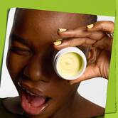 Model, ki namiguje, s posodico Kiehl's Creamy Eye Treatment z avokadom, ki prekriva jedno oko