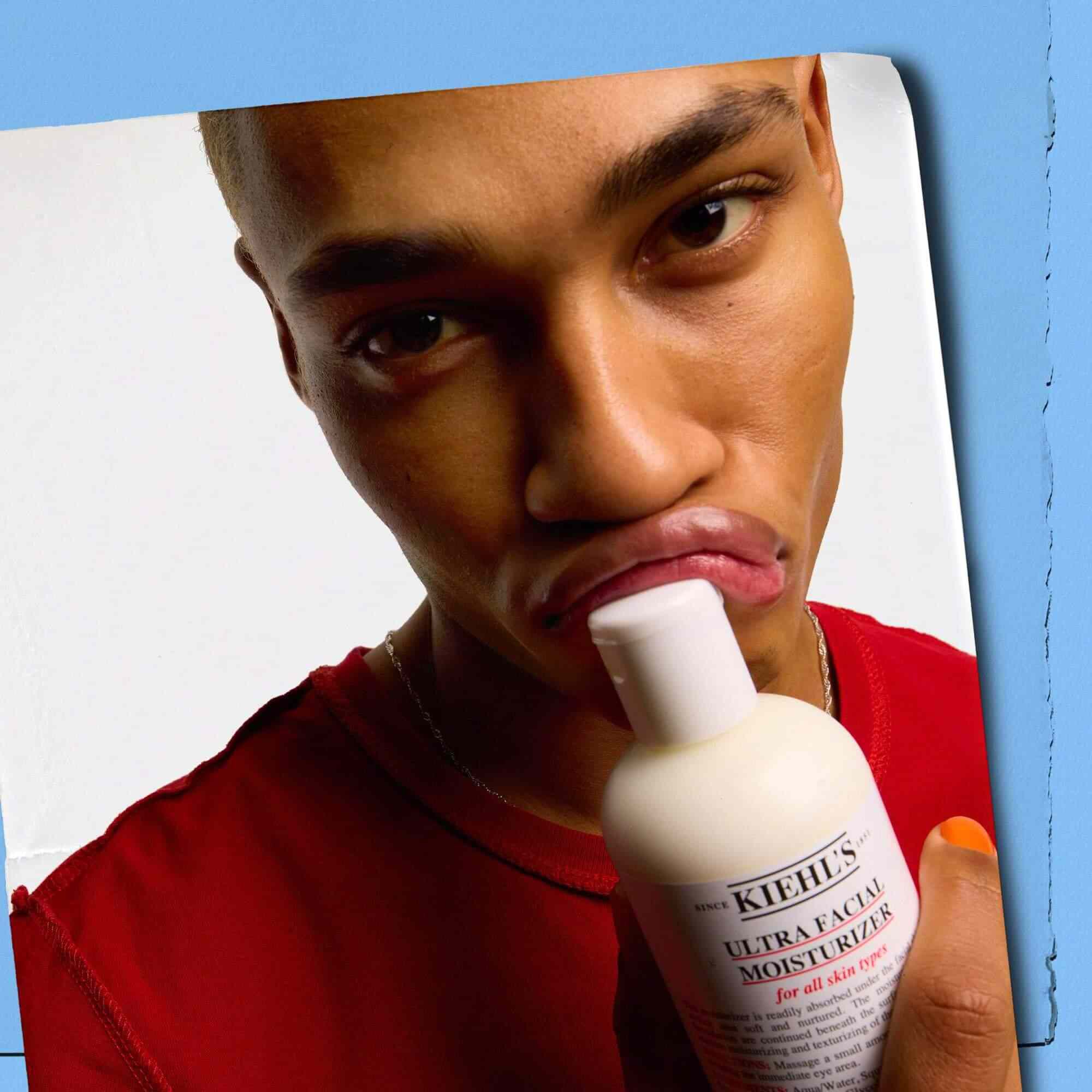 Model, ki stekleničko Kiehl's Ultra Facial Moisturizer pritiska na svoje ustnice