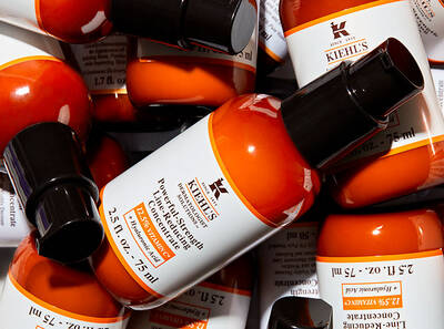 Serum Kiehl's v oranžnih stekleničkah, razporejen med belimi nalepkami z navodili, v osrednjem fokusu.