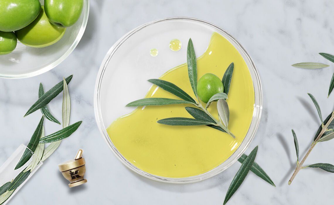A clear dish with a smooth, vibrant green olive oil or dressing, accompanied by fresh olives and olive leaves, set against a marble background.