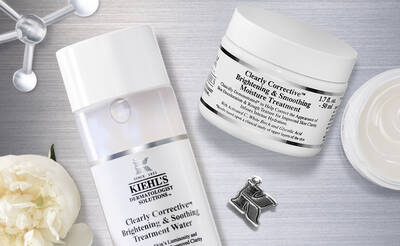 A flat lay image featuring skincare products from Kiehl's: a bottle of Clearly Corrective Brightening & Smoothing Treatment Water and a jar of Clearly Corrective Brightening & Smoothing Moisture Treatment, surrounded by a delicate flower and a silver pin.