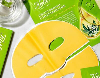 Zelena embalaža Kiehl's maske za obraz z rumeno masko in steklenico, razporejena na marmorni podlagi.