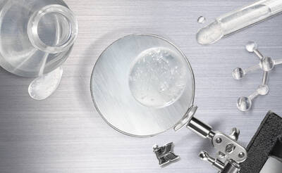 A magnifying glass focusing on a droplet of water, surrounded by a glass vial, a test tube, molecular models, and a clip stand, all set against a metallic background.