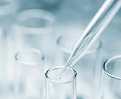 A close-up image of a pipette poised above a row of clear test tubes, with a soft, blurred background.