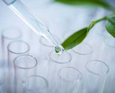 A glass dropper releasing a droplet of liquid above multiple test tubes, with a green leaf nearby.