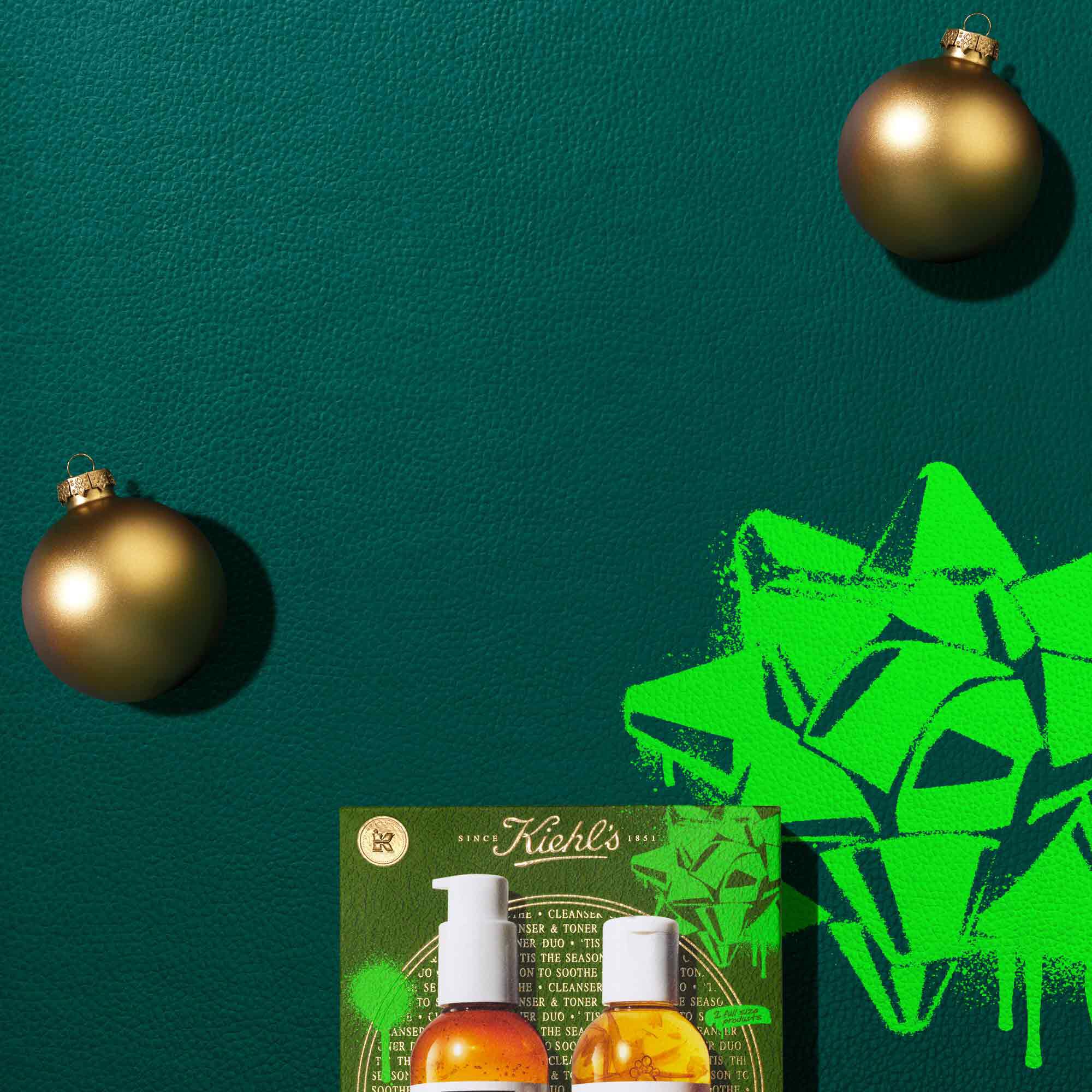 A graphic, set against a dark green background with bright green accents, features two bottles of Kiehl’s Calendula Deep Cleansing Foaming Face Wash and Calendula Herbal-Extract Toner, both with clear packaging and amber-colored liquid. The bottles are arranged above a festive green and gold Kiehl’s gift box displaying the same two products. Two gold ornaments are also part of the arrangement.