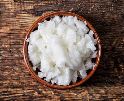 A clay bowl filled with fluffy, white coconut coir or texture, sitting on a rustic wooden surface.