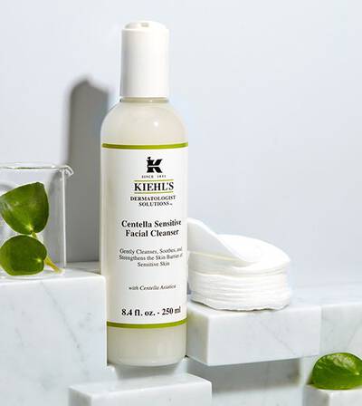 Čistilec za obraz Kiehl's Centella Sensitive v steklenički na marmorni površini, obdan z vatiranimi blazinicami.