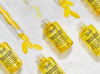 Stekleničke Kiehl's Daily Reviving Concentrate z rumenim oljem in cvetnimi listi na belem marmorju.
