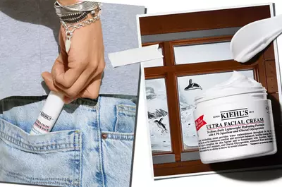 A close-up of a hand holding a travel-sized Kiehl's Ultra Facial Cream, with a background featuring a jar of the cream and a scenic winter landscape visible through a window.