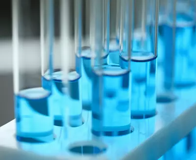 Close-up of test tubes filled with vibrant blue liquid, arranged in a white rack with soft lighting.
