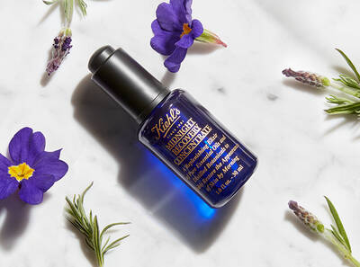 Steklenička modre nočne kreme z rožicami in zelišči okrog, imenovana 'Midnight Recovery Concentrate.'