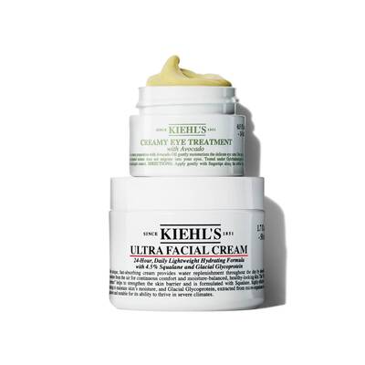 A jar of Kiehl's Ultra Facial Cream atop a jar of Kiehl's Creamy Eye Treatment with Avocado, both showcasing their distinctive white and green packaging.