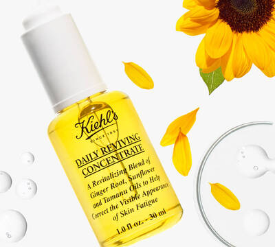 Kielh's Daily Reviving Concentrate v steklenički z rumeno vsebino in sončnicami v ozadju, namenjen oživljanju kože.