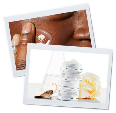 Close-up of a hand applying exfoliating scrub on dark skin, alongside skincare jars with floral accents.
